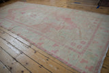 Distressed Oushak runner at an angle, displaying its sprawling medallion and soft pink and sand hues.