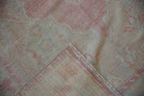 Folded corner of a distressed Oushak rug reveals the hand-knotted back and low pile.