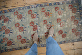Feet on distressed Oushak runner, showing faded rose bouquets and blue border.