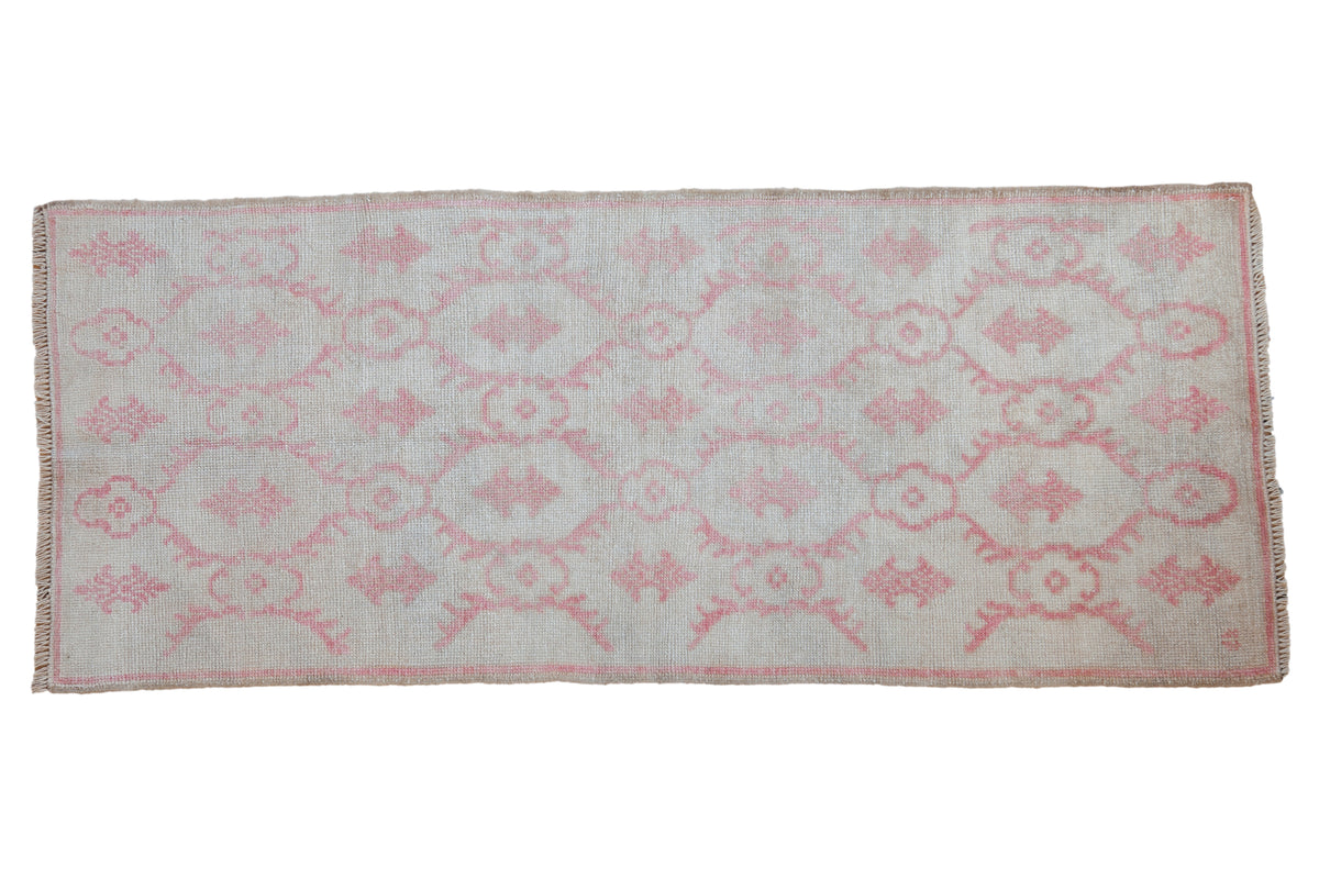 Vintage distressed Oushak runner with an allover floral pattern in pale raspberry red on an antique ivory field.