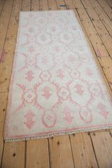 Angled view of a vintage Oushak runner's distressed low pile and pale raspberry red pattern.
