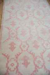 Angled view of the worn knot heads and pale raspberry floral motifs on a distressed Oushak runner.