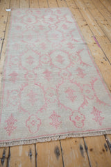 The full length of a vintage distressed Oushak runner viewed from an angle, showcasing its faded raspberry red pattern.