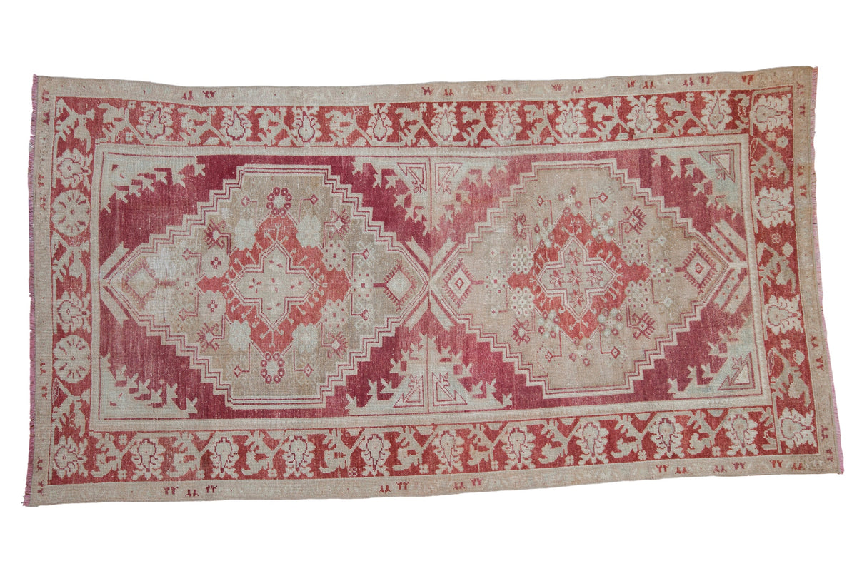 Vintage distressed Oushak carpet with stepped double medallions in faded cochineal red and ivory.
