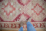 The time-worn texture and low pile of a distressed Oushak carpet with red geometric patterns.