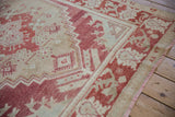 Corner view of a vintage Oushak rug showing its cochineal red floral border and worn texture.