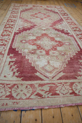 Angled view along a distressed Oushak carpet showing worn, stepped red geometric medallions.
