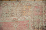 Textured close-up of vintage Oushak rug showing distressed raspberry, mint, and tangerine plant motifs.