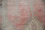 Distressed vintage Oushak rug showing faded raspberry, cream, and seafoam green scrolled vines.