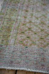 Worn texture of a vintage distressed Oushak rug, featuring soft pale cochineal and lime green hues.