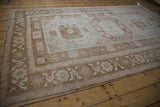 Distressed Oushak rug corner, low pile, fringed edge, with pale copper and blush stylized blossoms.