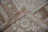 Distressed Oushak rug folded, revealing low pile, fringe, selvage, and hand-knotted foundation.