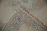 Vintage Distressed Oushak carpet folded corner, showing faded cream pile, green, mauve border motifs, fringe.