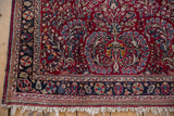 Corner of a vintage Sarouk rug showing its pinwheel floral border and ivory fringe.