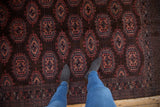 Feet on vintage Turkmen rug, dark brown field, copper gul medallions, checkered border.