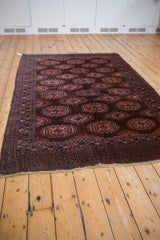 Angled view of the vintage Turkmen rug showing staggered gul medallions on its dark chocolate brown field.