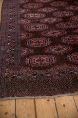 Dark chocolate brown field with ram's horn gul medallions, geometric border, and fringed edge.
