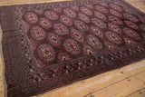 Turkmen rug's bottom corner showing dark chocolate brown field, gul motifs, and checkered outer border.