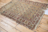 Antique Caucasian rug corner, displaying worn saffron field, terracotta floral motifs, and tattered fringe.