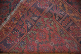 Madder red, navy blue geometric lattice with botehs and vines on antique Qashqai rug, showing tattered edge.