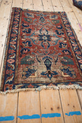 Persian Lilihan rug corner showing worn cherry red field, navy floral border, and fringe.