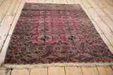 Close-up of antique Turkmen rug: repeating floral guls, abrashed dusty magenta field, intricate navy and burgundy borders, even pile wear.