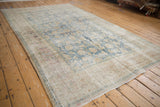 Distressed Persian Meshed rug at an angle, showing exposed foundation and faded blue palmette designs.
