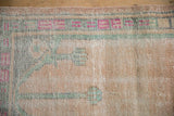 Geometric floral border in magenta and pale mint green on the distressed, apricot pile of a vintage Oushak mat.