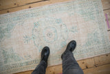 Worn pile of vintage distressed Oushak runner with faded cream and dusty jade green designs.