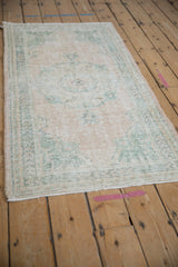 Distressed vintage Oushak runner showcasing faded cream and dusty jade green floral motifs.