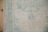 Distressed Oushak runner's worn pile texture with faded cream and dusty jade green hues.