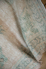 Visible wear to knot heads and foundation of the cream and faded green Oushak rug pile.