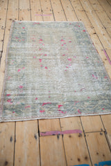 Distressed Oushak rug texture, showing fuchsia geometric blossoms and visible wear.