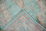 Distressed Oushak rug's fold reveals worn pile, ocean green selvage, and hand-knotted foundation.