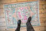 A distressed vintage Oushak rug with fuchsia and teal accents, shown on the floor for scale.