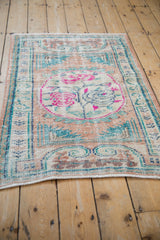 Angled view of a distressed Oushak rug showing its low pile texture and fuchsia accents.
