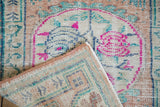 A folded corner reveals the back weave of a distressed Oushak rug with fuchsia and teal details.