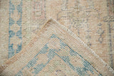 Distressed vintage Oushak rug pile with cream, blue, and blush tones, showing intact side selvage.