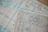 Distressed Oushak runner's worn cream, green pile revealing foundation, with reverse weave and fringe.