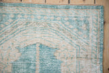 Corner detail of a distressed Oushak rug with seeded spandrels in ocean green and cream.