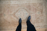Distressed Oushak rug's central hexagonal medallion on abrashed sand, cream, and faint blue ground.