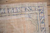 Distressed Oushak rug detail, pale sand field, worn cobalt blue vine border.