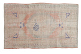 Vintage distressed Oushak rug with a roundel medallion in faded rose, seafoam, and navy on a worn ivory field.