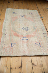 Angled view of a distressed Oushak rug with a faded rose medallion and worn, low-pile texture.