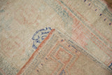Folded corner of a distressed Oushak rug showing its hand-knotted foundation and low, worn pile.