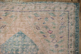 Pale rose distressed Oushak rug texture with scattered seed motifs and visible knot heads.