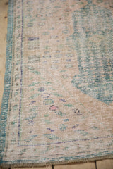 Distressed Oushak rug corner showing wear to foundation, pale rose and green seed motifs, turquoise selvage.