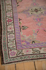 Distressed vintage Oushak corner with pink field, lavender serrated border, seafoam accents, and fringe.