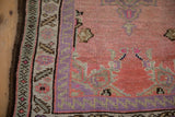 Distressed vintage Oushak rug's serrated purple border, sea foam green floral band, pink field.