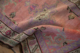 Distressed Oushak rug's folded texture, highlighting pink, purple, and green floral borders.